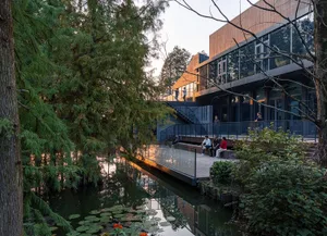 A waterfront building with a glass facade, benches, and chairs, surrounded by water and offering a relaxing atmosphere