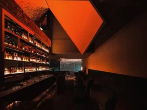 Modern bar area with a counter featuring bottles and chairs, wine glasses, and a stylish atmosphere