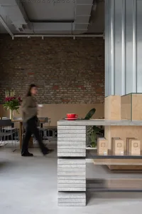 A rustic cafe interior with a brick wall, potted plants, and a counter with displayed items and cups