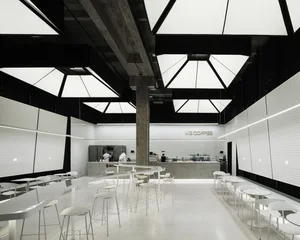 A modern coffee shop interior with multiple tables and chairs, steel, and glass, warm and inviting atmosphere