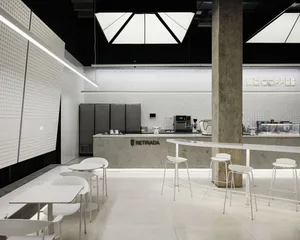 Modern restaurant interior with white walls, grey floors, and dining tables, chairs, and appliances