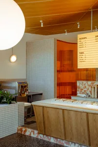 Modern restaurant kitchen with a counter featuring a drink machine and refrigerator, two sinks, and various items and potted plants