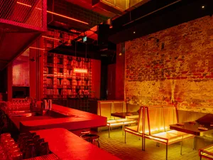 A warm and inviting bar area with red walls, chairs, a dining table, and bottles, perfect for socializing and enjoying meals