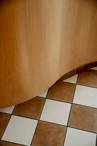 A brown wooden door with a curved design stands in front of a tile floor with a checkered pattern, creating a warm and inviting atmosphere