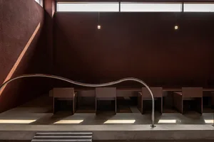 A modern restaurant interior with a curved wall, multiple tables, and comfortable seating for guests, well-lit by natural and artificial light