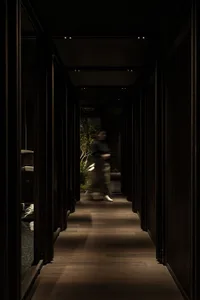 A hallway with wooden floors and walls, featuring two people walking and engaged in conversation