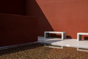 A stone bench in front of a red wall creates a visually appealing and inviting outdoor patio area for relaxation or socializing