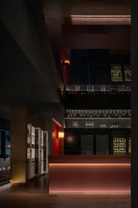 A sophisticated bar area with a long countertop, wine glasses, and bottles, set against a backdrop of red walls and wooden accents