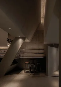 Modern open kitchen and dining space with concrete walls and floors, featuring two chairs and a minimalist aesthetic