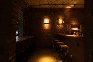 Cozy bar area with a brick wall, wooden stools, and three chairs around a bar counter