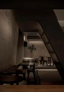 Open industrial space with concrete walls and floors, featuring chairs, dining tables, potted plants, and decorative elements