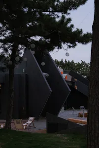 Black exterior building with a large window, several chairs, and two dining tables in an outdoor gathering or event space