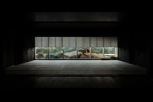 An empty room with large windows, natural light, and several rocks arranged within the space