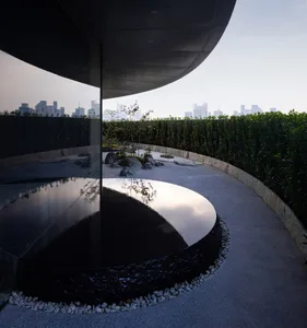 A modern building with a large circular window on its side, reflecting the surrounding environment, with a combination of glass and stone elements