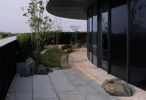 A modern patio with a glass door, rock garden, small waterfall, and potted plants, creating a serene atmosphere with natural elements
