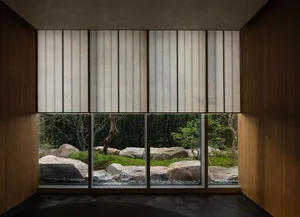 A living area with a large window offering a view of a garden, surrounded by potted plants and natural light