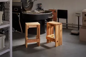 Industrial kitchen with wooden stools, small tables, and a coffee maker on a concrete floor