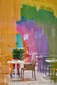 A modern restaurant interior with a dining area, bar, and colorful curtains, surrounded by potted plants