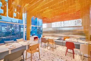 A cozy restaurant dining area with multiple wooden tables, chairs, and potted plants, creating an inviting atmosphere for a meal