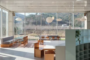 Modern restaurant interior with wood flooring, glass walls, and numerous dining tables and chairs