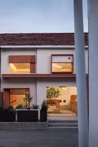 A modern house with a red roof, large window, and balcony, surrounded by greenery and a warm atmosphere