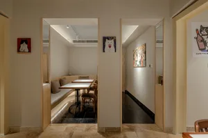 Modern living space with a dining table, chairs, couch, and bench, surrounded by a white color scheme and two doors leading to other areas