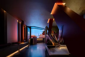 A modern hotel lobby with a mix of red and white elements, featuring potted plants and a vase, set in a spacious area with natural light from a large window