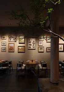 Warm and inviting restaurant interior with tables, chairs, framed pictures, and a central tree, surrounded by natural elements and artistic decorations