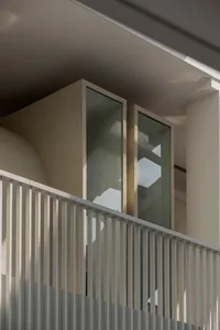 A modern building with a white exterior and two large windows, one of which is a glass door, adding depth and interest to the structure