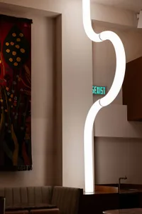 A modern room with a large white wall featuring a green sign reading sexist, a curved light, and a painting on the wall