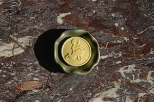 A green ceramic bowl sits on a brown, textured marble countertop with a yellow design in the center of the bowl
