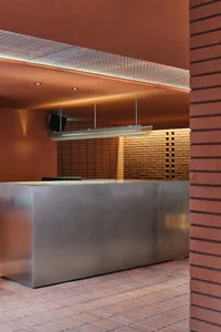 Industrial kitchen with a large silver countertop, two sinks, and a hanging lamp providing illumination