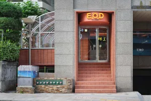 A modern building with a red brick facade, large window, and two doors, set in a contemporary urban environment