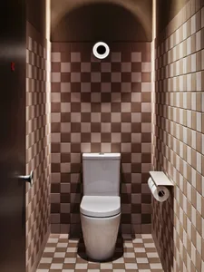 Small bathroom with a white toilet, brown tile walls, and a sink in the background