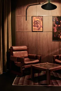 A cozy living room with two leather chairs, a wooden table, and a painting on the wall, creating a warm and inviting atmosphere