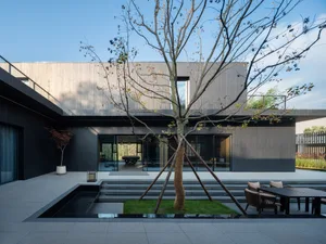 A modern house with black walls, a glass door, and a tree in front, featuring two chairs and a dining table outside