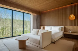 Well-lit bedroom with a large window, a bed, two couches, a chair, and a dining table, creating a modern and inviting atmosphere