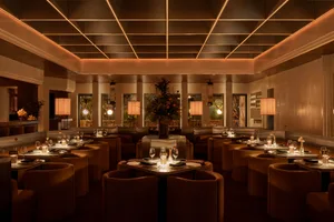 Warm and inviting restaurant interior with multiple tables, chairs, potted plants, and wine glasses on brown and white modern furniture