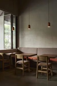 A modern restaurant interior with gray walls, dim lighting, and a cozy atmosphere, featuring a dining area with tables, chairs, and benches