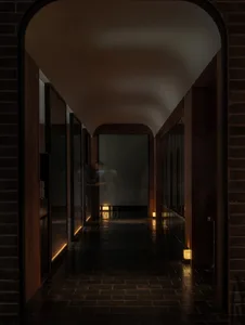 A dark hallway with a black tile floor, featuring two people standing at the end, with no windows or natural light