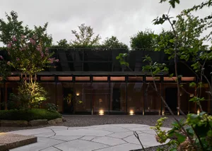 A modern building with a glass facade surrounded by trees and bushes, featuring large windows that allow natural light into the interior spaces