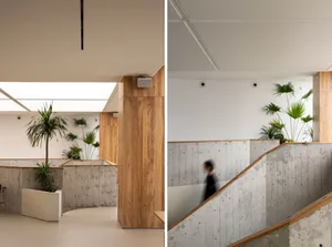 A building interior with a staircase, potted plants, and three people in different areas of the space
