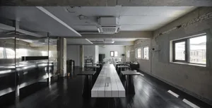 A clean and well-organized dining area with a long white table, multiple chairs, and potted plants, set in a commercial building