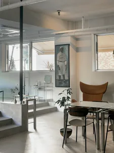 Open living area with white walls and floors, featuring chairs, a dining table, potted plant, and vase, well-lit and inviting