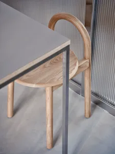 A cozy indoor space with a wooden chair on a grey carpet in front of a table, featuring a modern metal-framed chair