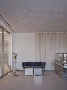A modern living space with a couch, chair, dining table, and vase, surrounded by white walls and curtains, with a comfortable and inviting atmosphere