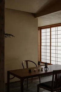 A dining area with a wooden table and chairs, surrounded by natural light from a window, creating a warm and inviting atmosphere
