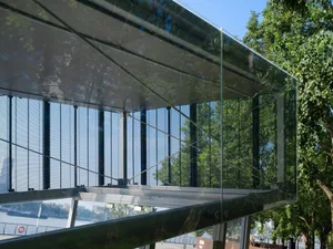 Exterior photo of a modern building with a glass facade, multiple windows, and a natural background with trees