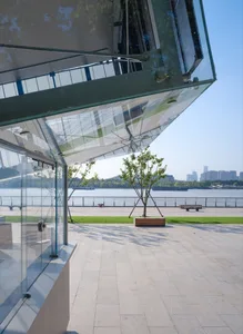 A modern building with a glass roof and large glass wall, featuring benches and boats in the background