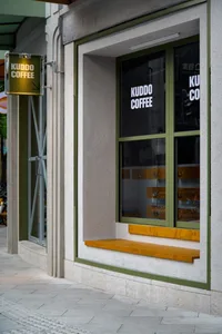Exterior view of a coffee shop with a wooden bench and green frame, surrounded by bicycles and inviting atmosphere